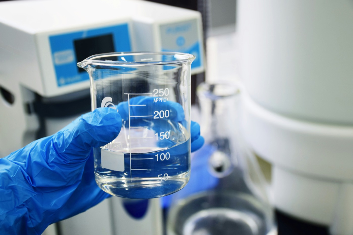 Gloved hand holding a graduated laboratory beaker of reagent